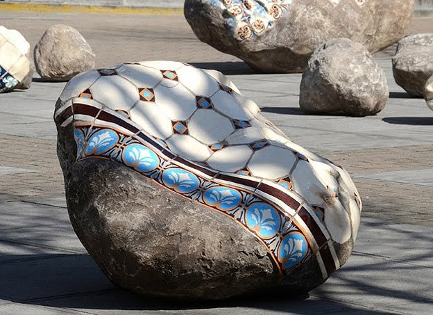 a rock sitting on top of a sidewalk next to large rocks