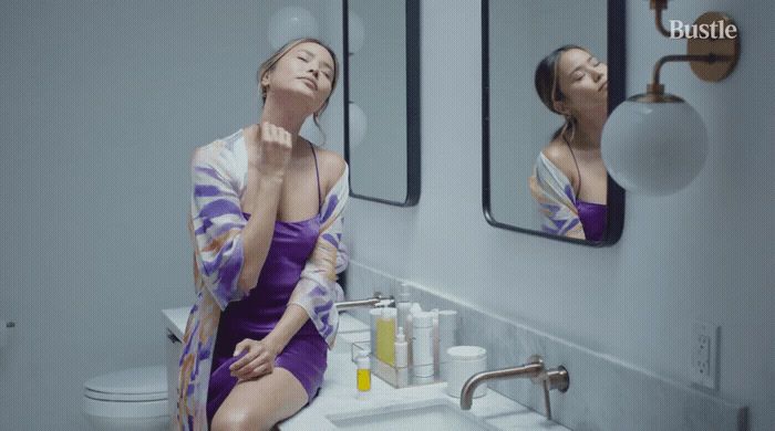 a woman in a purple dress sitting in front of a bathroom mirror