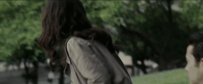 a woman walking down a street next to a lush green park