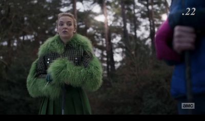 a woman in a green fur coat standing in front of a forest