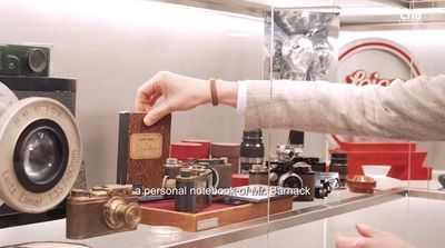 a person holding a small box in front of a display of old cameras