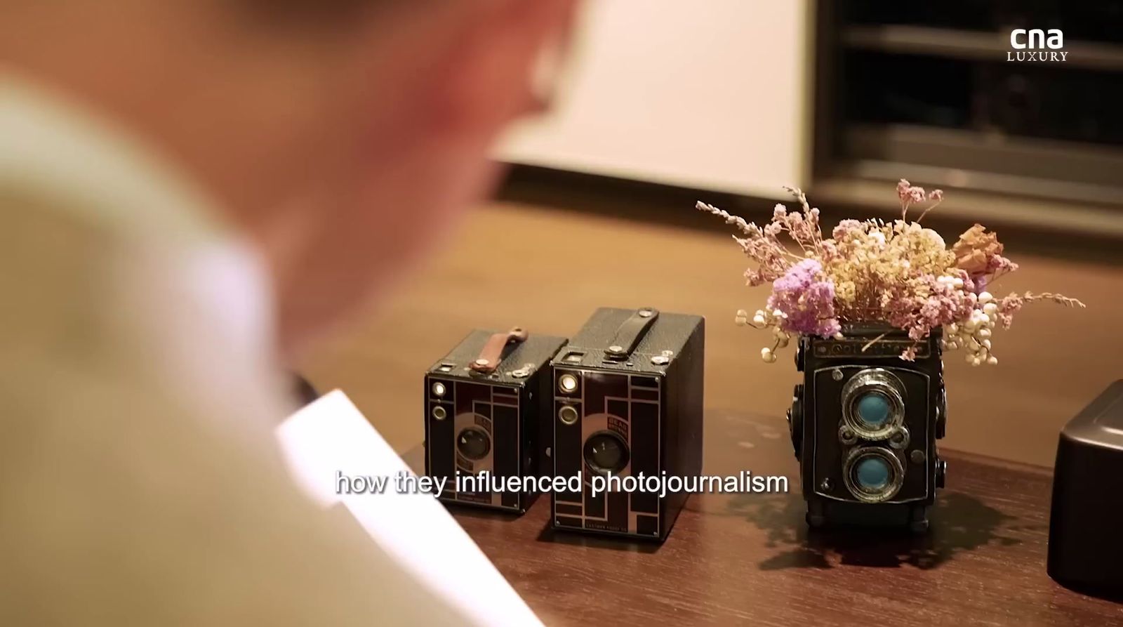 a man looking at three old cameras on a table