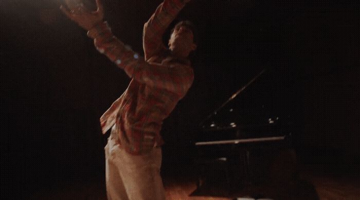 a man standing in front of a piano in a dark room