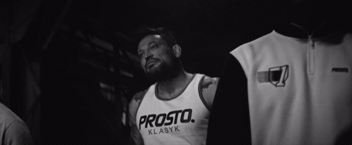 a black and white photo of a man standing in front of some shirts