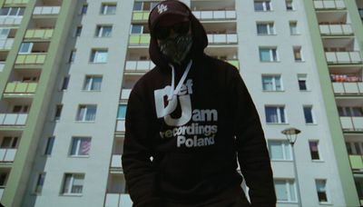 a man in a hoodie standing in front of a tall building