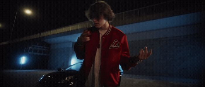 a man in a red jacket is walking towards a car