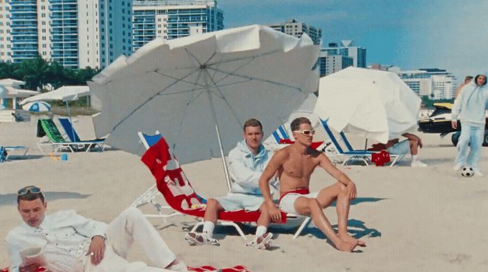 a group of men sitting on top of a sandy beach