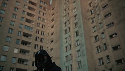 a man in a hoodie standing in front of tall buildings