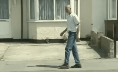 a man walking down a sidewalk in front of a house