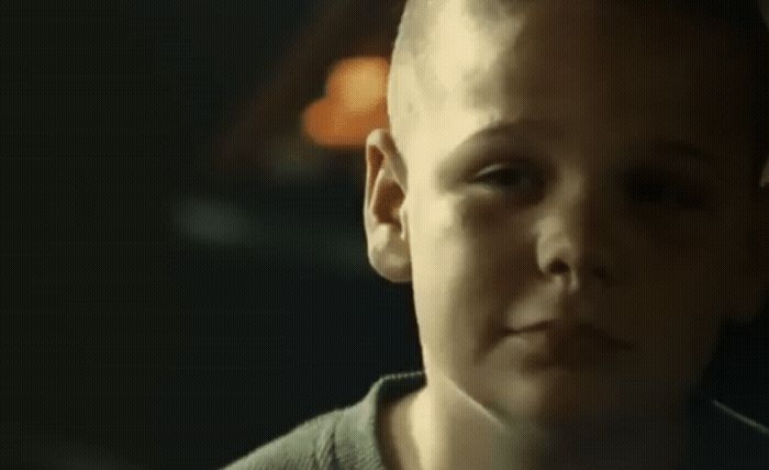 a young boy with a bald head stares into the distance