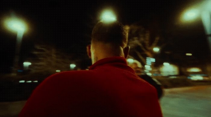 a man in a red jacket walking down a street at night