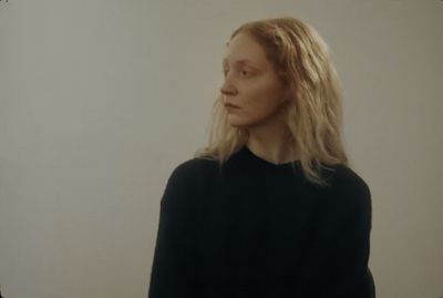 a woman with long blonde hair standing in front of a white wall