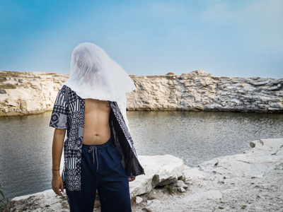 a man with a veil on his head standing near a body of water