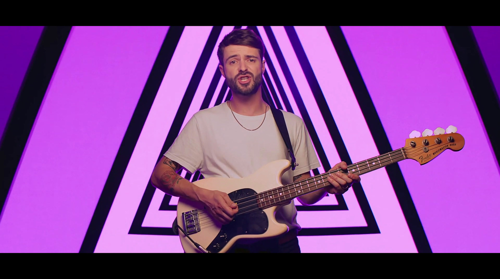 a man holding a bass guitar in front of a purple background