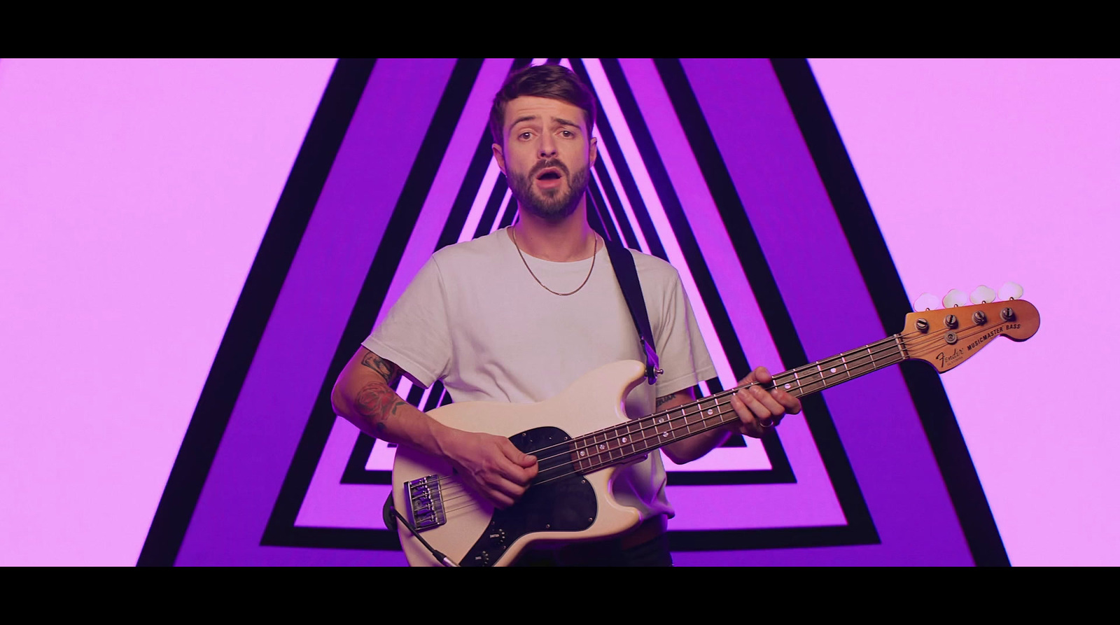 a man holding a bass guitar in front of a purple background