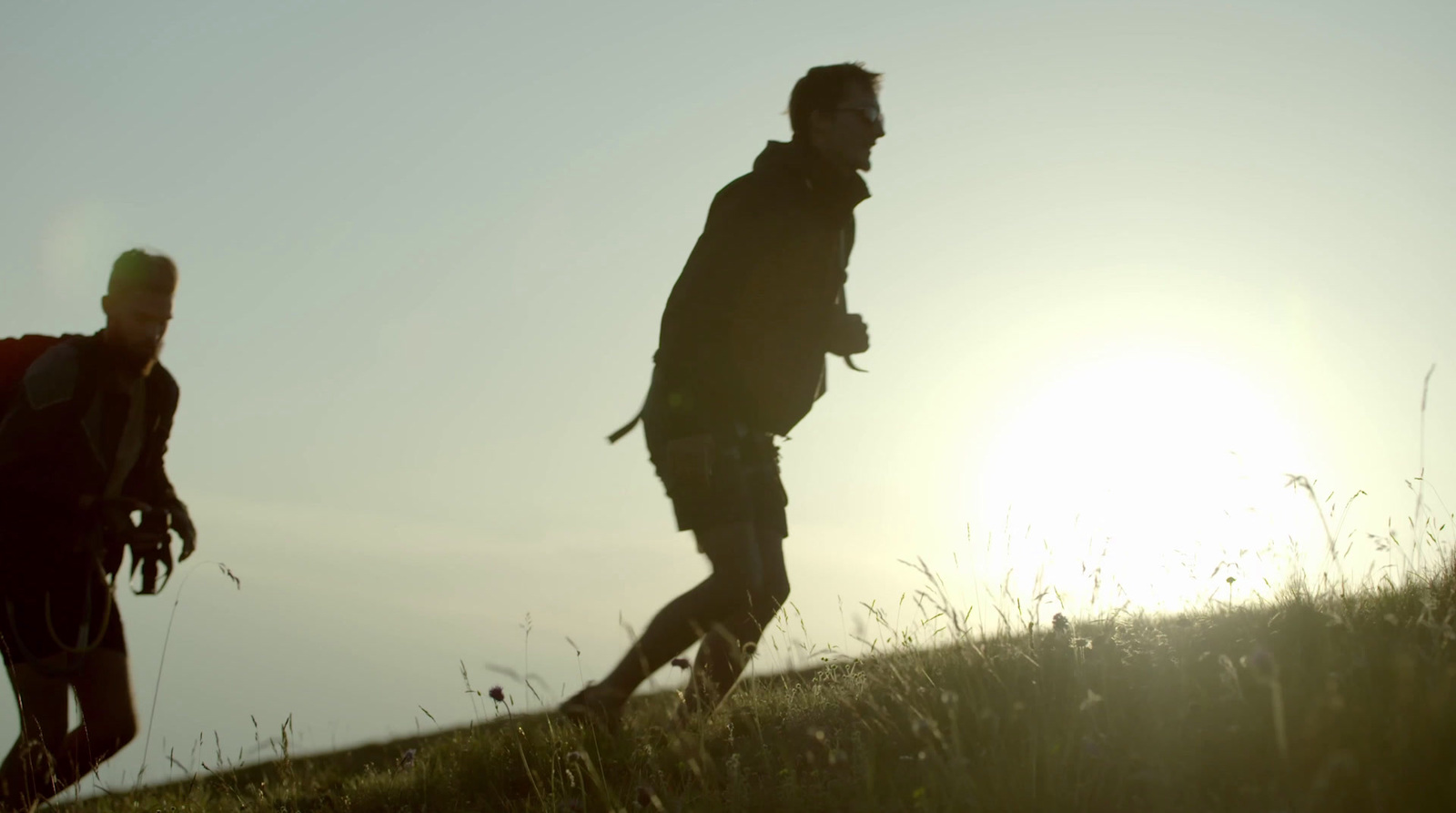 a couple of men walking across a grass covered field