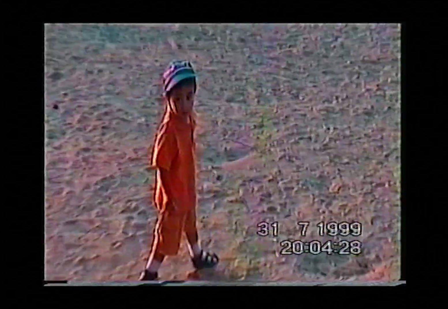 a small child in an orange jumpsuit standing in a field