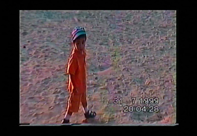 a small child in an orange jumpsuit standing in a field