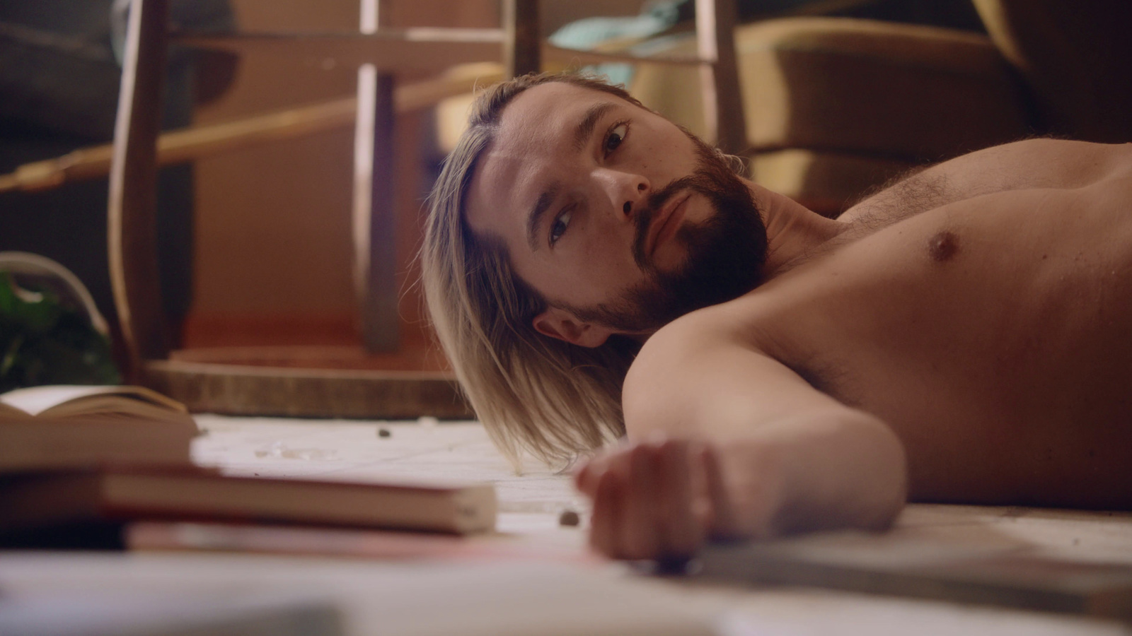 a shirtless man laying on the floor next to a book