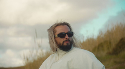 a man with long hair and sunglasses standing in a field