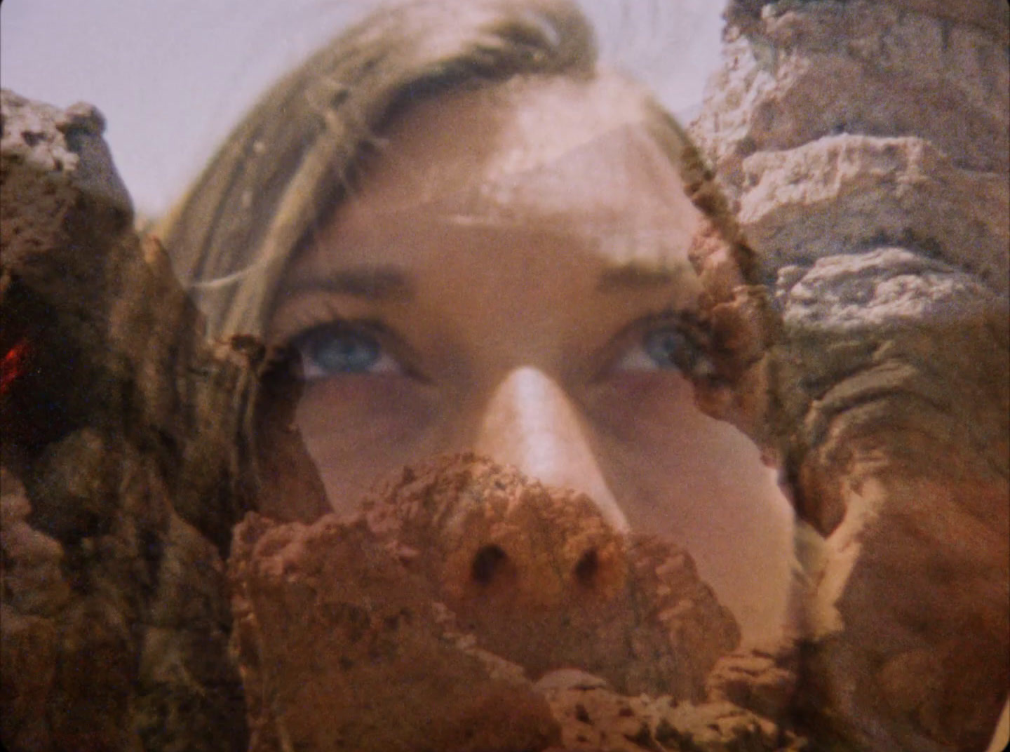 a close up of a woman's face behind rocks