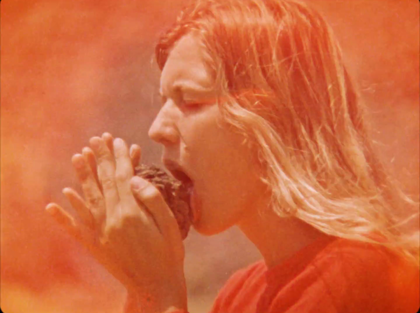 a man with long hair eating a doughnut