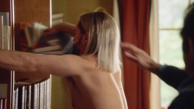 a shirtless man is reaching for a book in a library