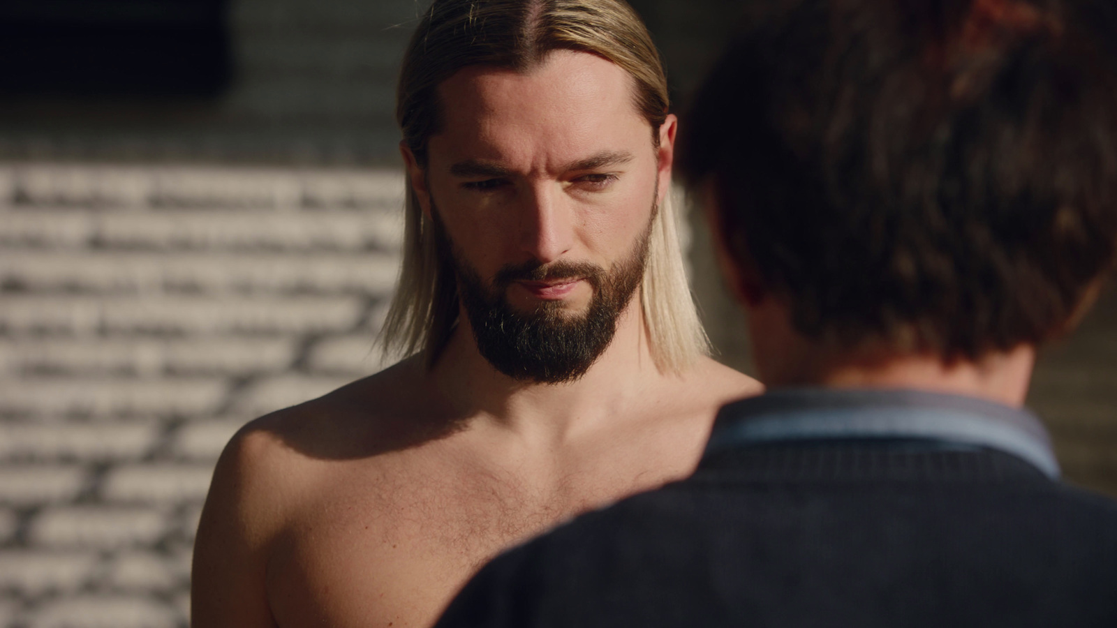 a man with long hair and a beard looking at another man