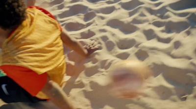 a young boy kicking a soccer ball on a sandy beach