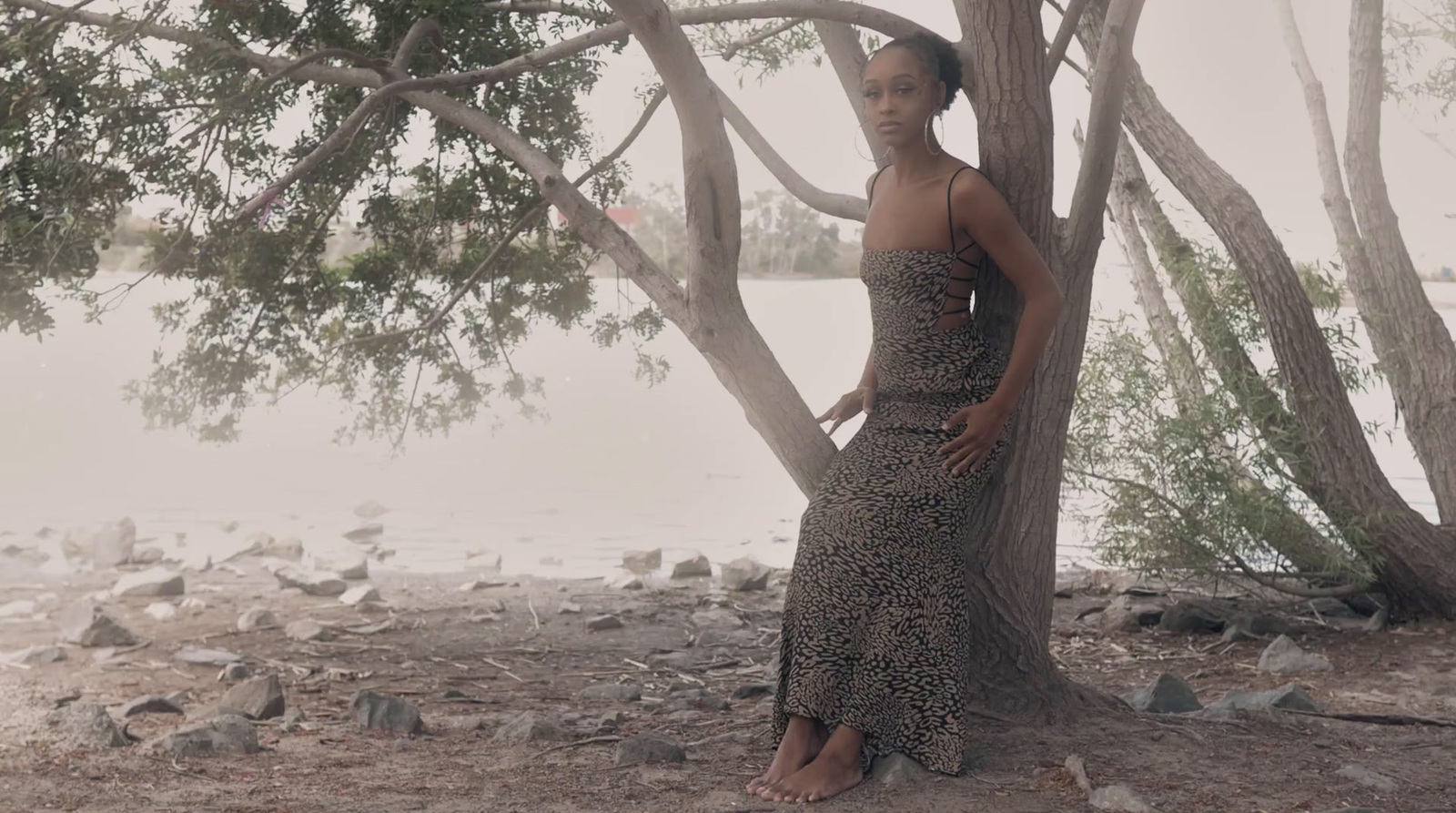 a woman standing next to a tree near a body of water