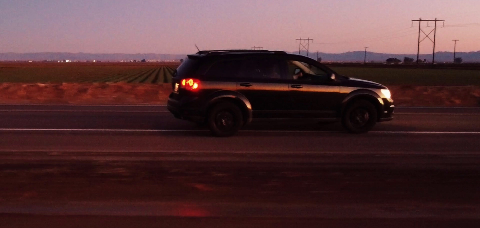 a black suv driving down a highway at dusk