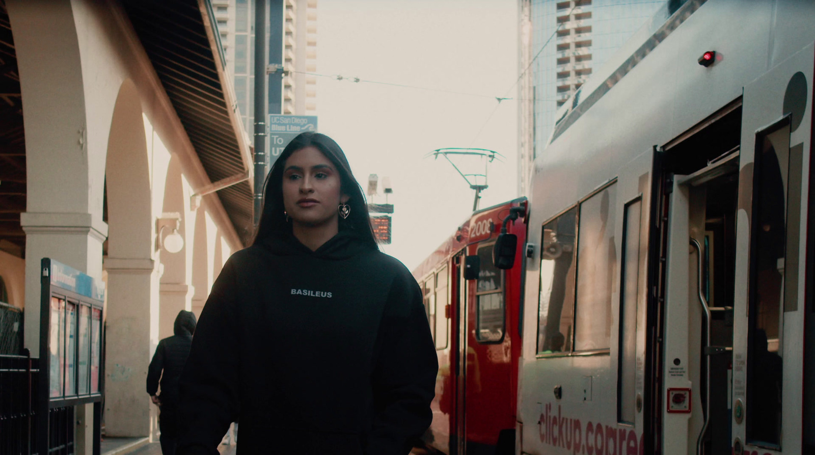 a woman in a black hoodie standing in front of a train