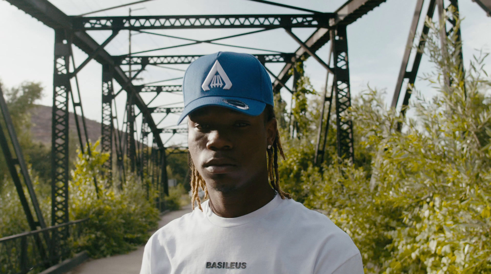 a man wearing a blue hat standing in front of a bridge