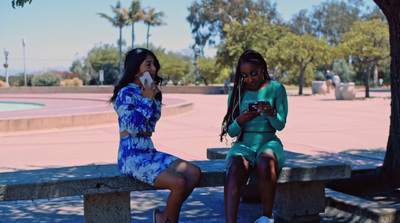 two girls sitting on a bench looking at their cell phones