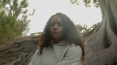 a woman with curly hair standing in front of a tree