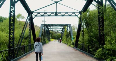 a woman walking across a bridge over a river