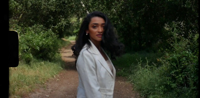 a woman walking down a dirt road next to a forest