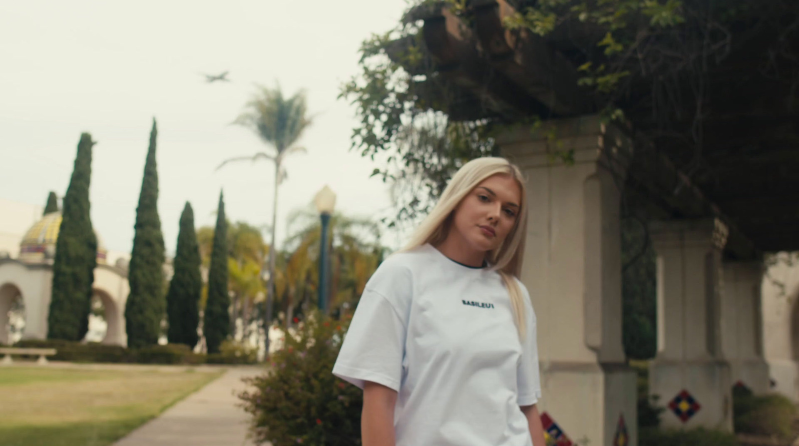 a woman in a white t - shirt standing on a sidewalk