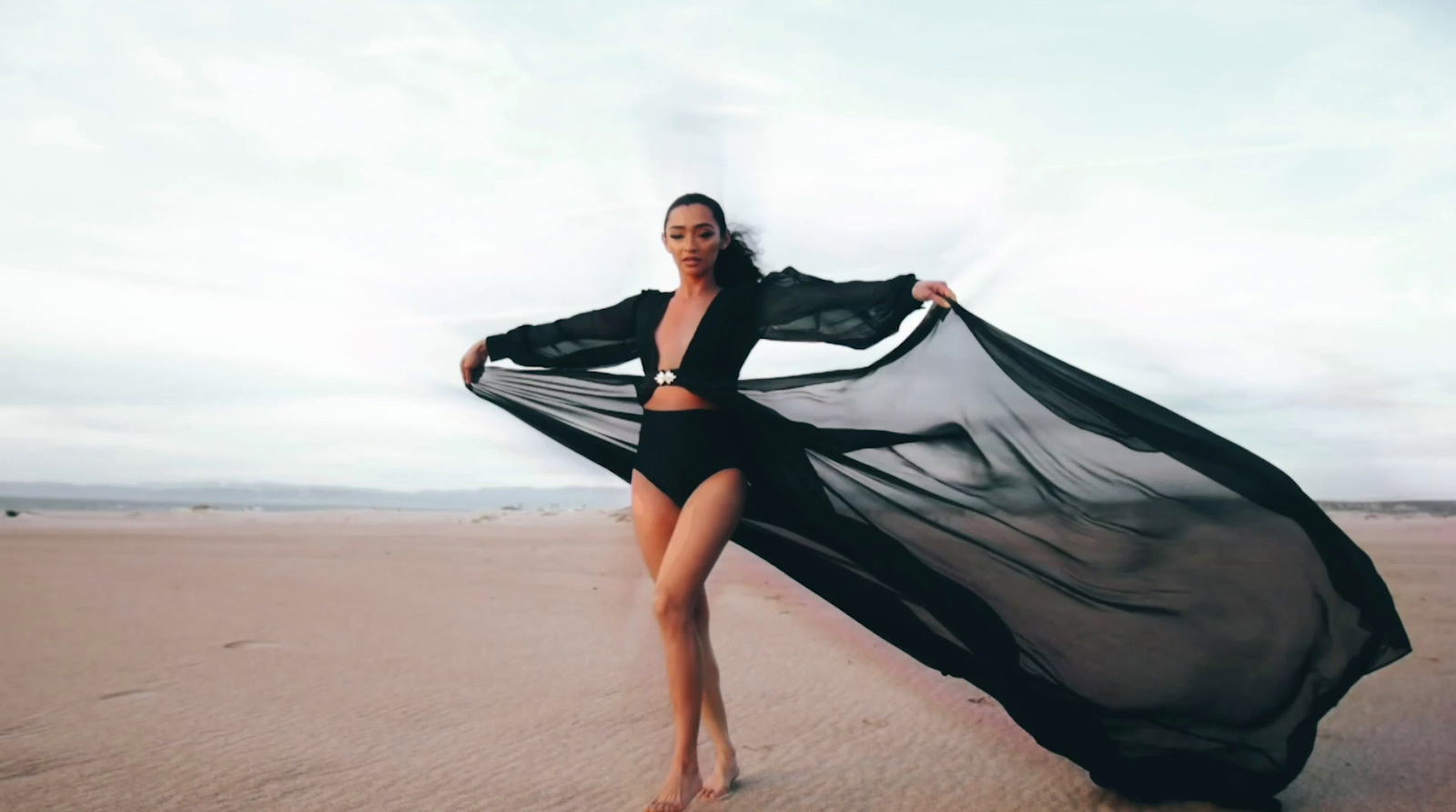 a woman standing on a beach holding a black dress