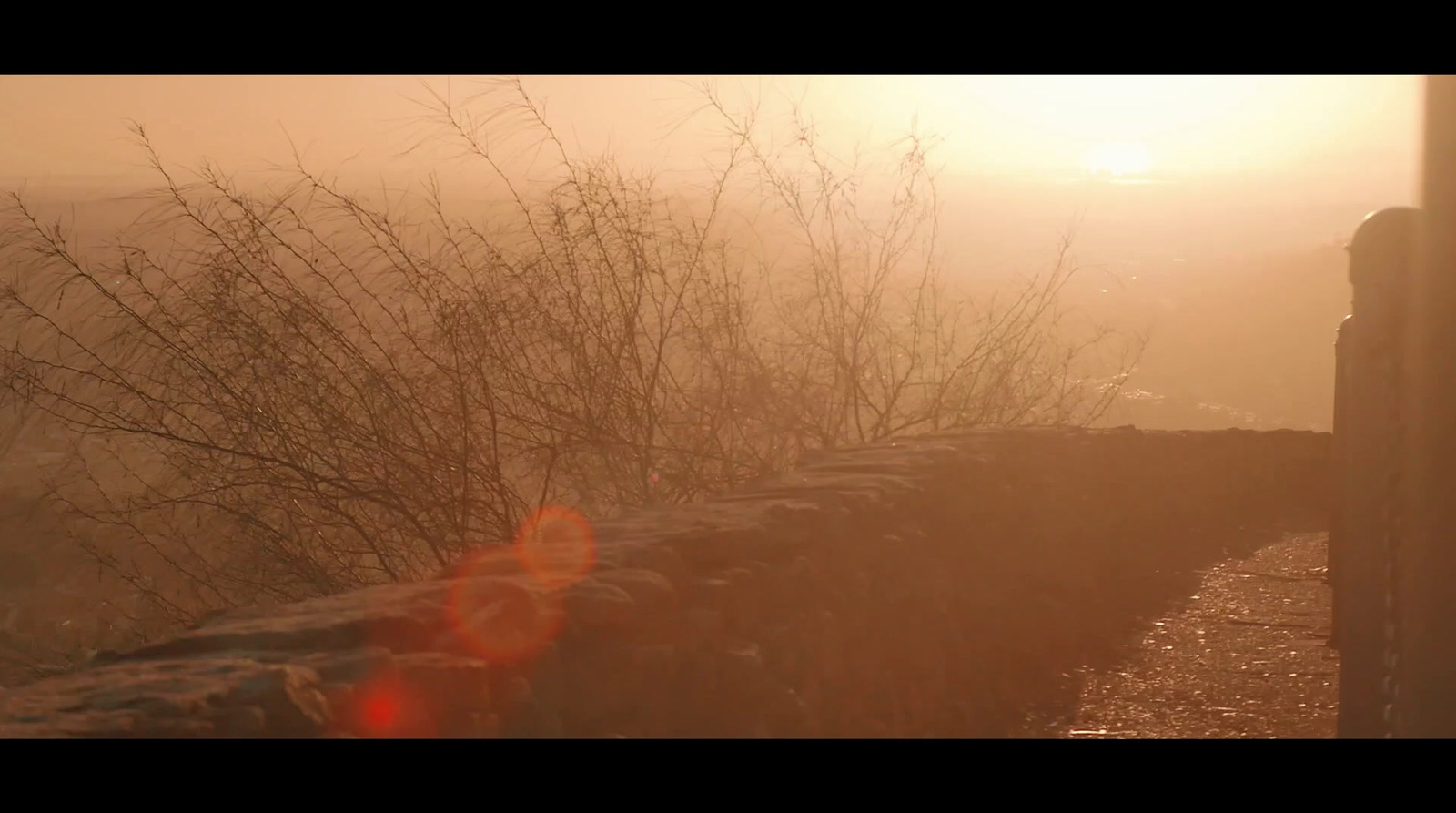 the sun is shining through the fog over a stone wall