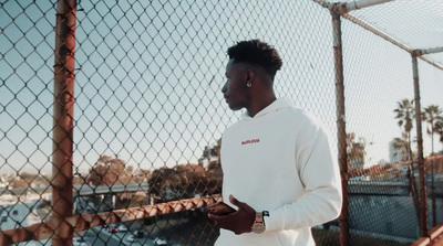 a man in a white hoodie standing by a fence