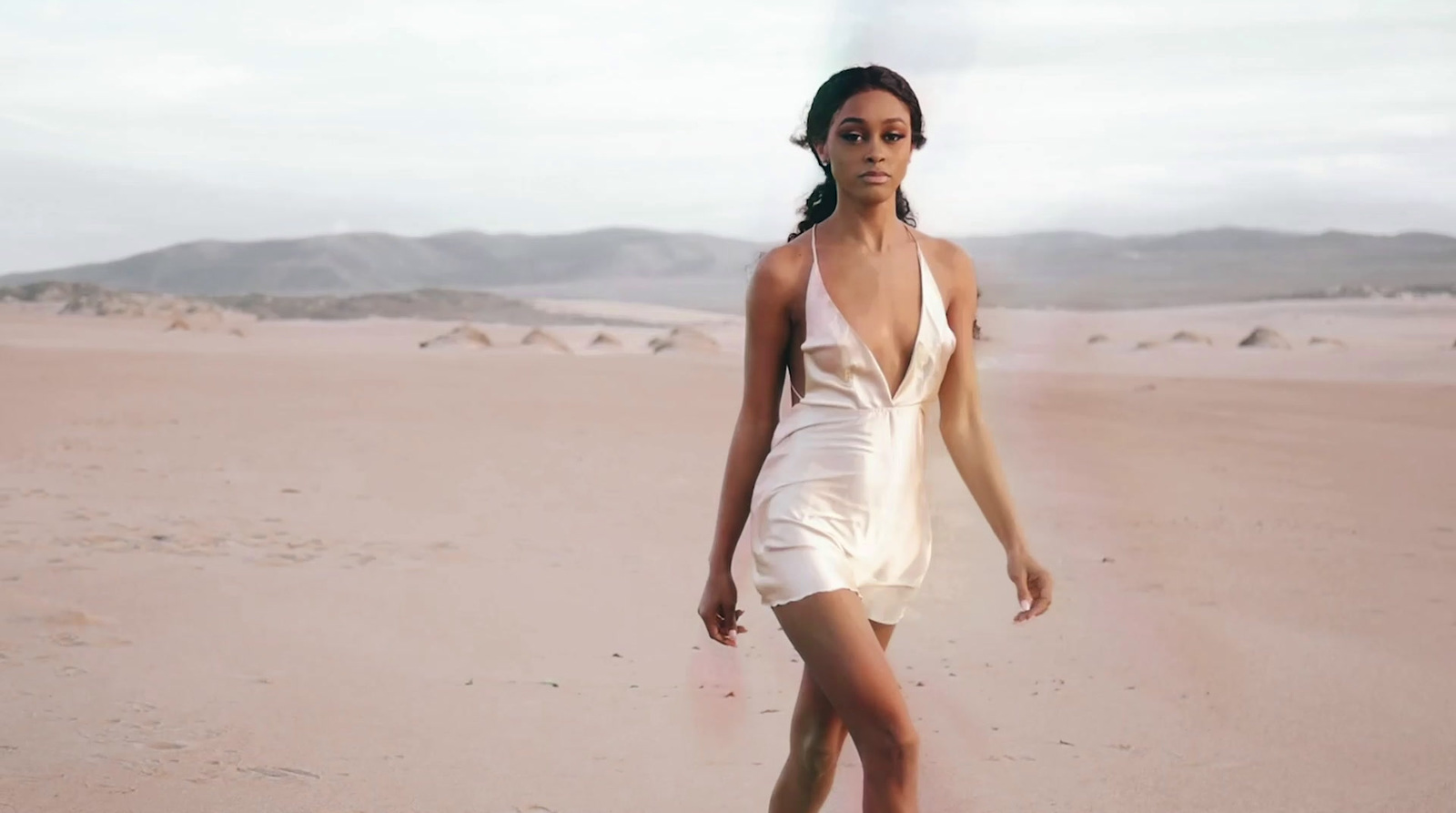 a woman in a white dress walking across a desert