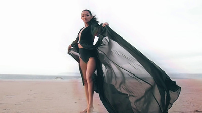 a woman standing on a beach holding a black dress