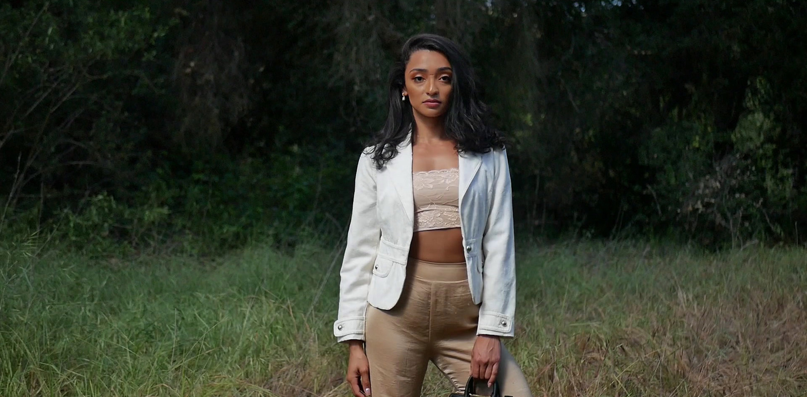 a woman standing in a field holding a purse