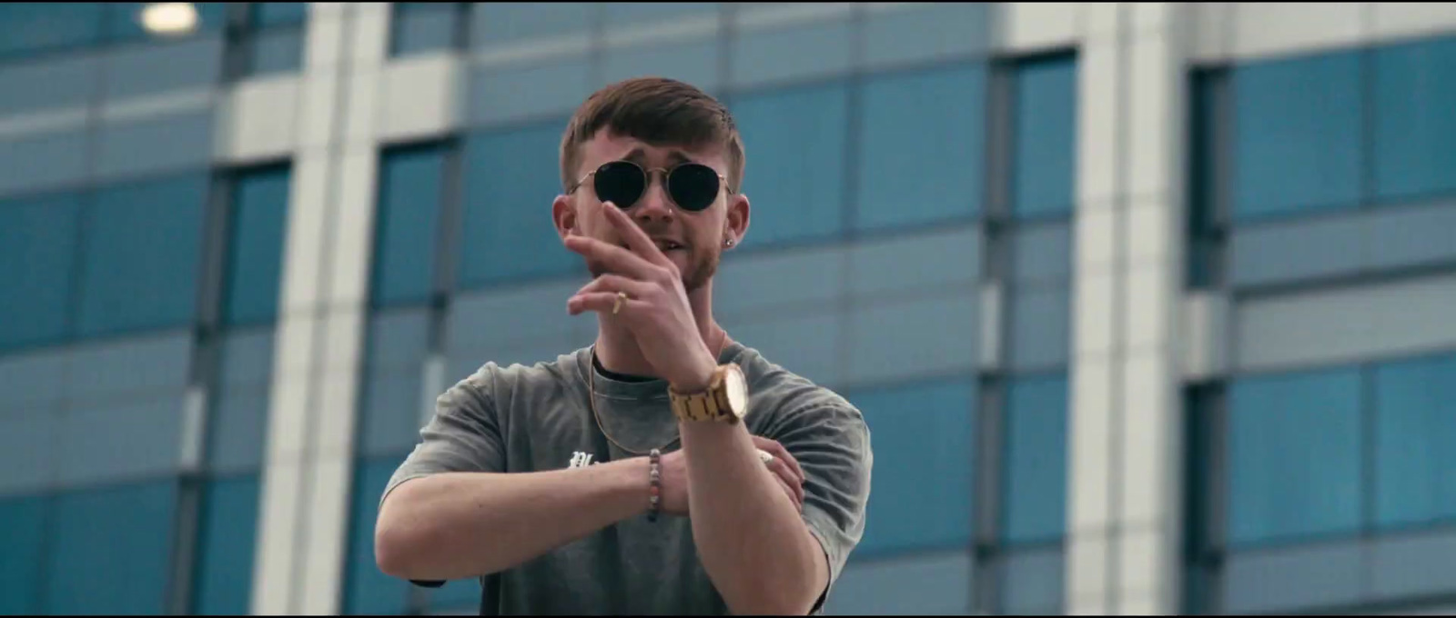 a man wearing sunglasses making a gesture in front of a building