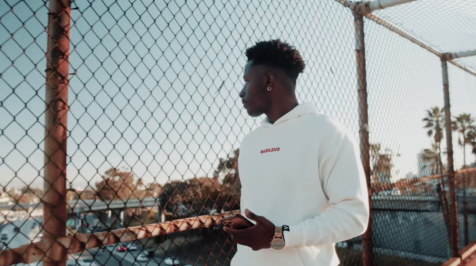 a man in a white hoodie standing by a fence