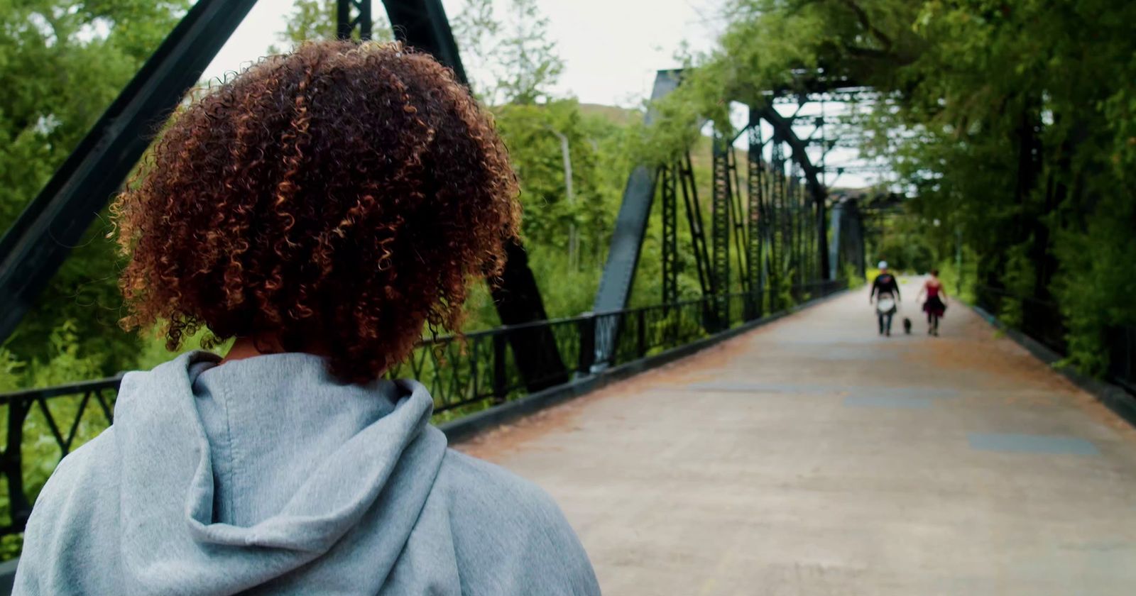 a woman with curly hair walking down a bridge