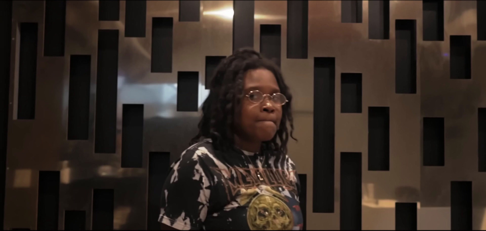 a woman with glasses standing in front of a metal wall