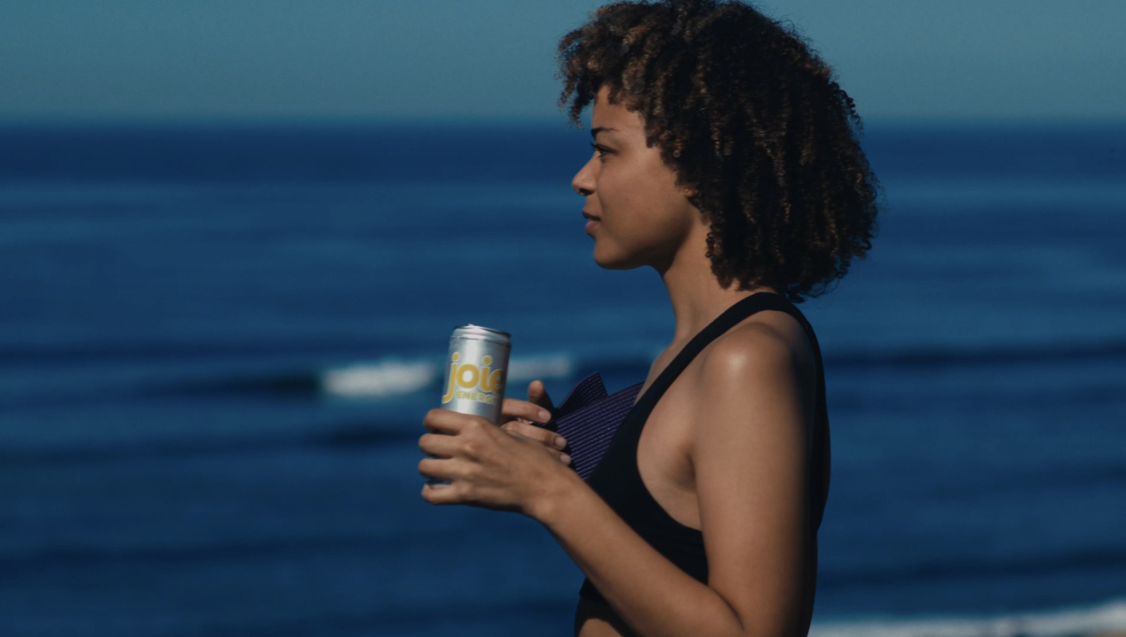 a woman holding a can of soda near the ocean