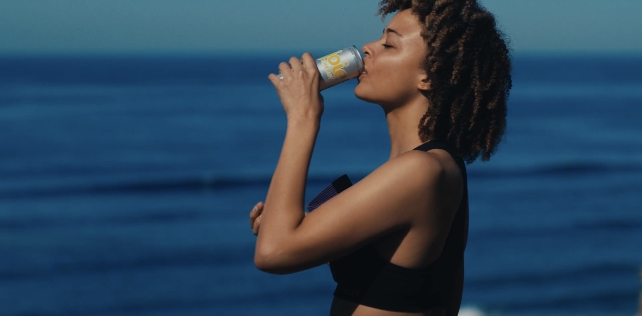 a woman drinking from a bottle near the ocean